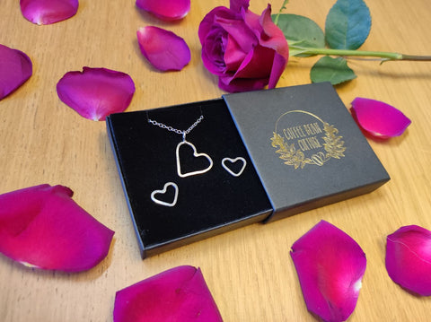 surrounded by roses are a gift set of hear earrings and necklace