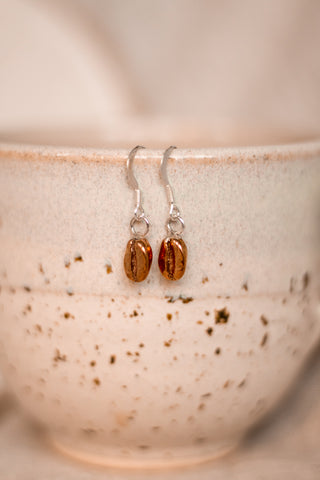 resting on a cup are a pair of red bronze coffee bean earrings