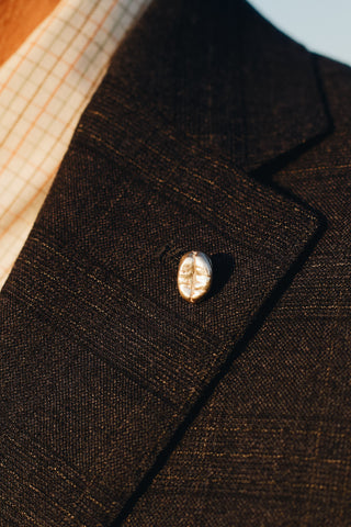 attached to a black suit jacket sits a sterling silver coffee bean badge