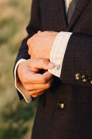 A man is holding onto his left sleeve to show off the sterling silver coffee bean cuff links he is wearing