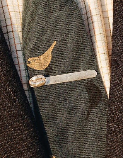 A sterling silver tie clip with a sterling silver coffee bean is attached to a green tie with a yellow bird design. 