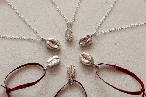 Six sterling silver coffee bean pendants are positioned in a star formation, each bean a different variety of coffee bean