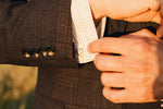 dressed in a suit stands a man holding a sterling silver coffee bean cuff link against his shirt