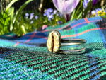 sitting upon a green tartan kilt sits a sterling silver coffee bean ring with a polished brass coffee bean