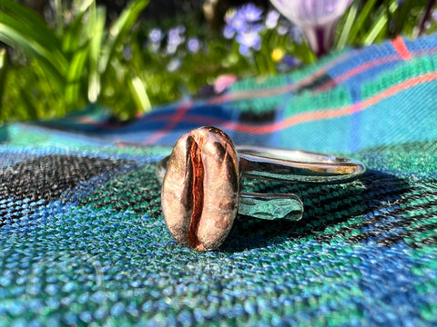 sitting on a green kilt sits a sterling silver ring with a red bronze coffee bean on it