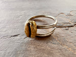 sitting upon a stone slate sits a sterling silver coffee bean ring with a polished brass coffee bean