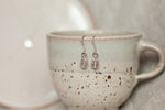 displayed on a mug sits a coffee bean earring set in sterling silver